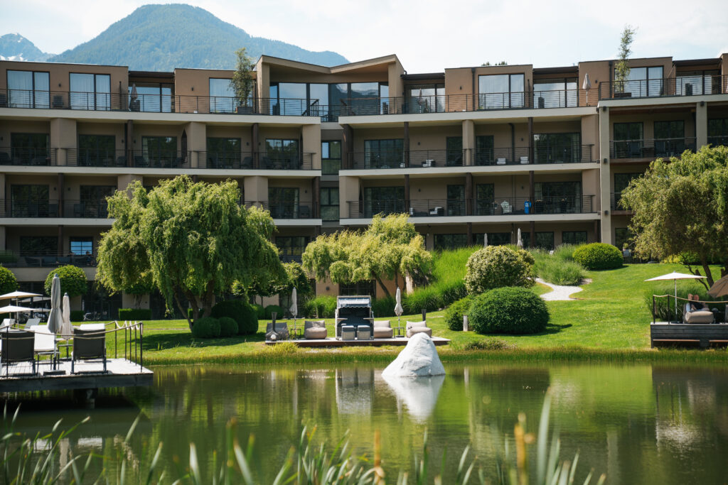 Select Green Hoteles Seehof Nature Retreat See mit grüner Liegewiese und Hotel im Hintergrund